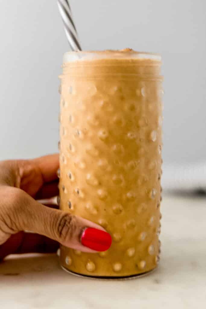 hand holding glass with pumpkin spice smoothie in it.