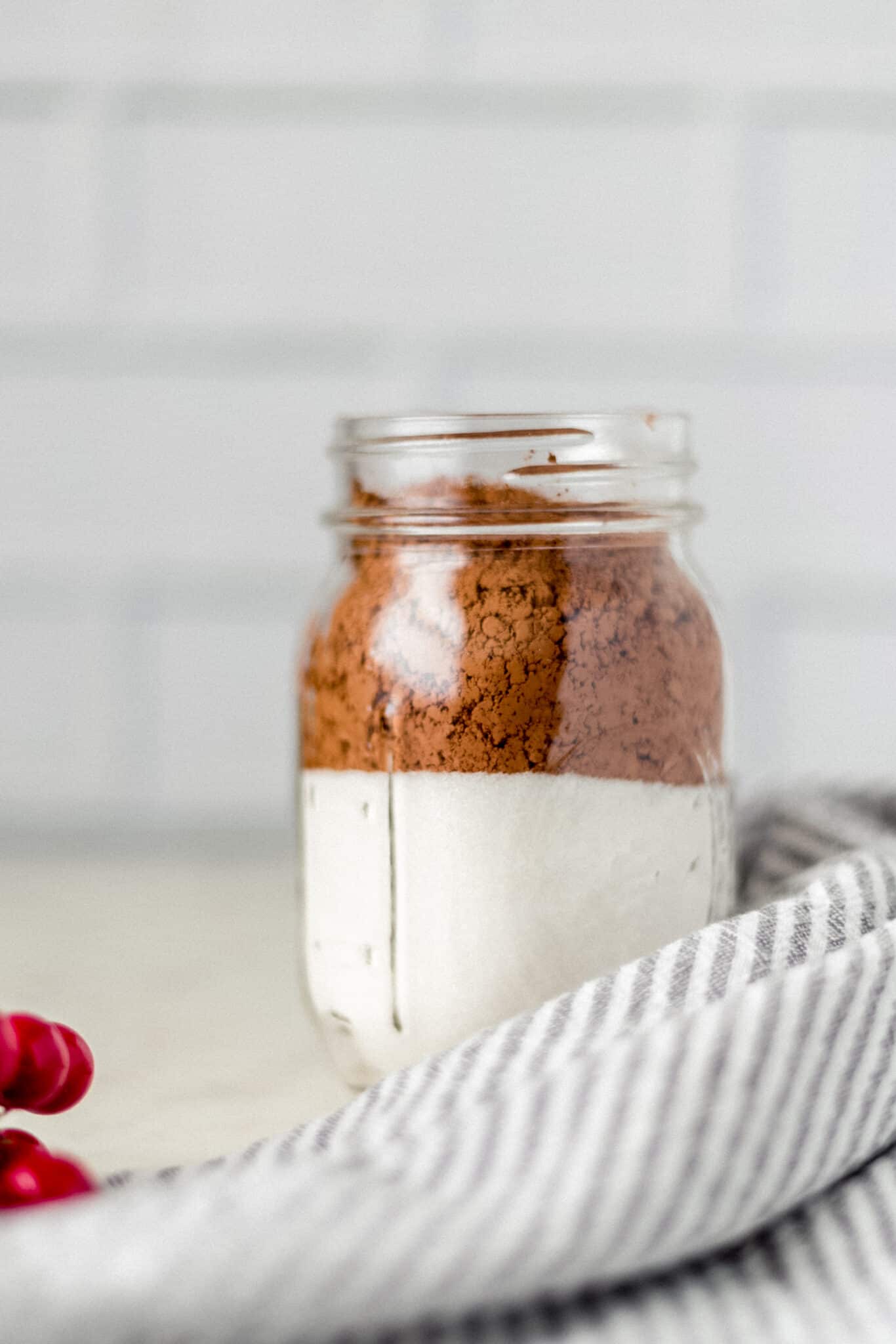 close up side view jar with cocoa powder and sugar in it next to a napkin