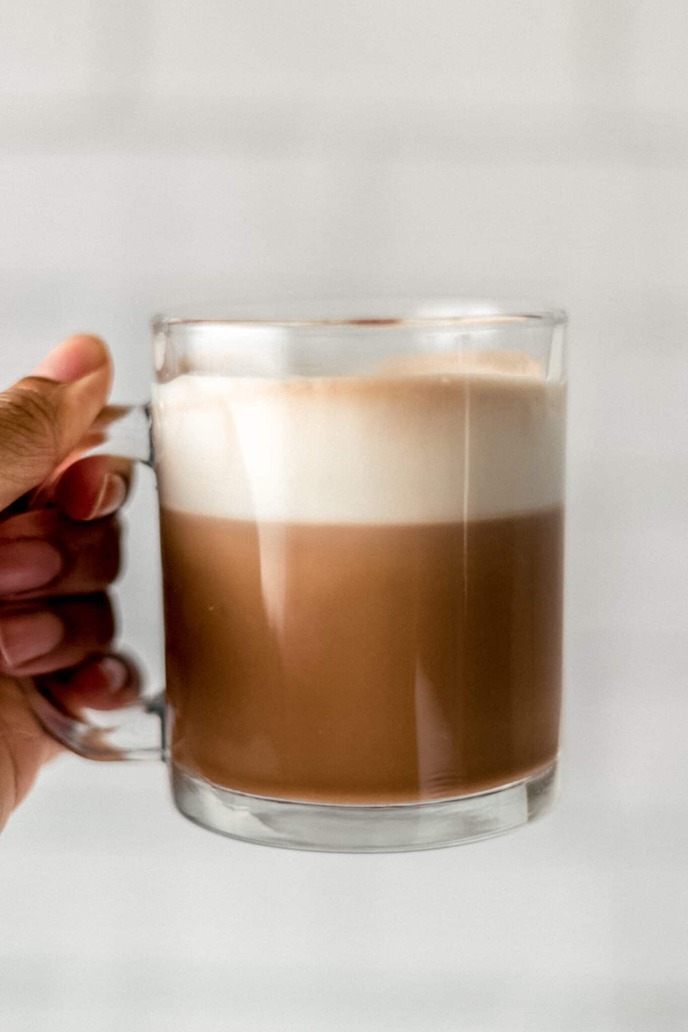 side view hand holding hand of glass mug filled with hot chocolate and topped with whipped topping