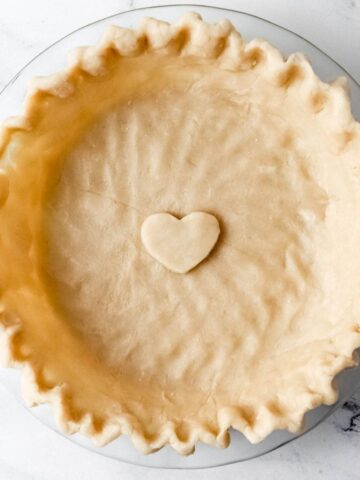 Overhead view of unbaked pie crust in glass baking dish on marble surface.