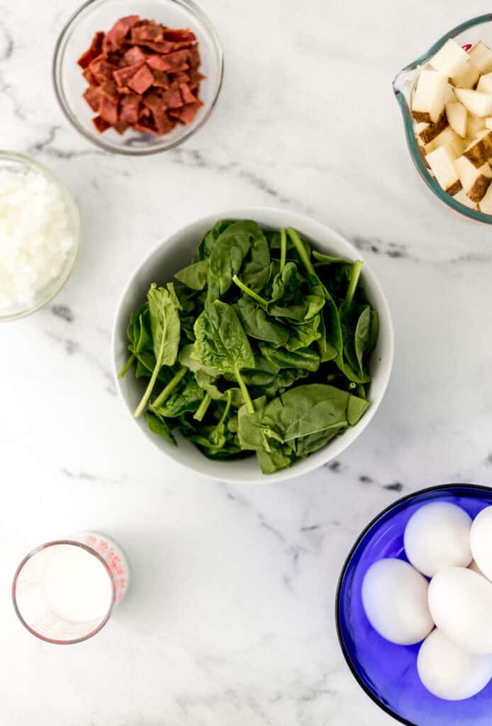 overhead view of ingredients needed to make frittata in separate containers on marble surface