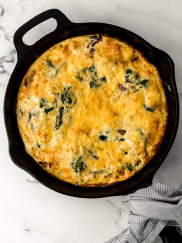 finished frittata in cast iron skillet with cloth napkin around handle