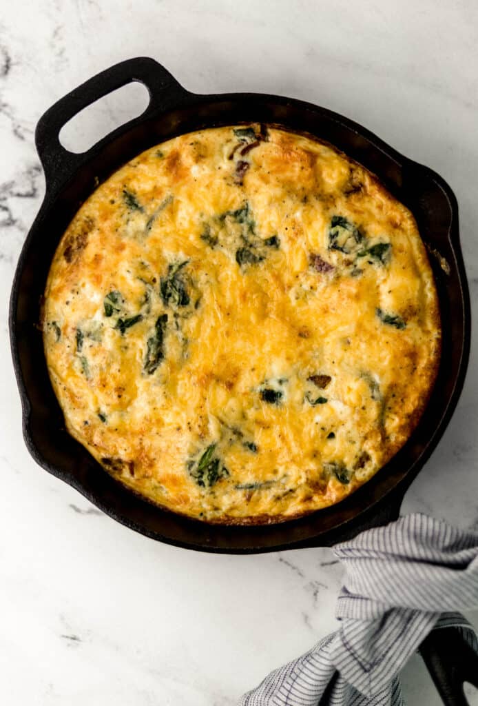 finished frittata in cast iron skillet with cloth napkin around handle