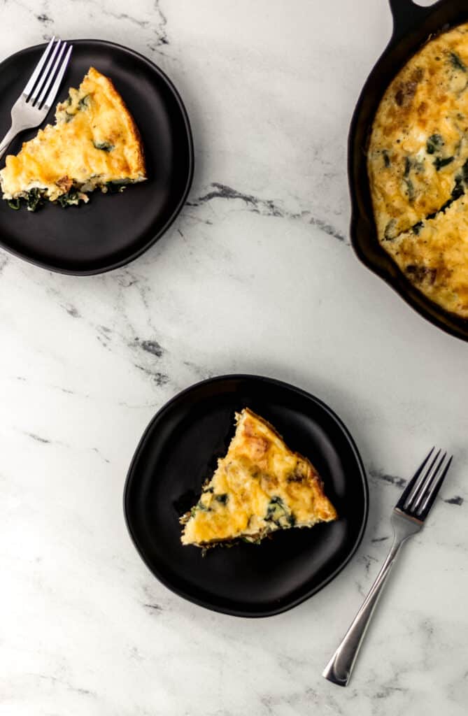 two pieces of baked frittata on black plates with forks 