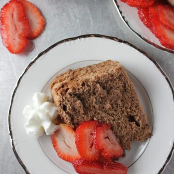 slice of cake on white plate with slices of strawberries and whipped cream