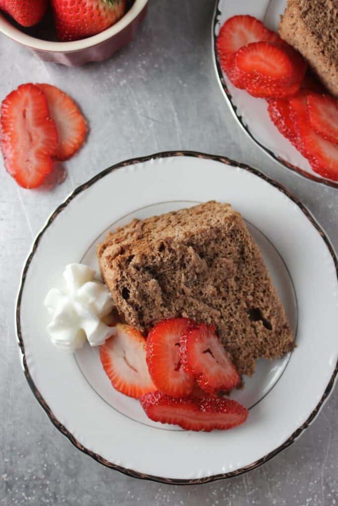 slice of cake on white plate with slices of strawberries and whipped cream 