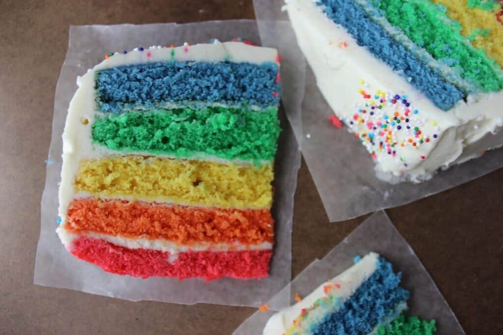 three slices of rainbow cake on wax paper 