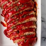 Overhead view of finished meatloaf sliced in white baking dish.