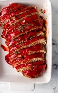 Overhead view of finished meatloaf sliced in white baking dish.