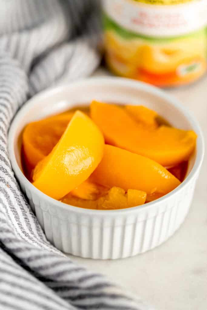 small white bowl with sliced peaches in it next to cloth napkin