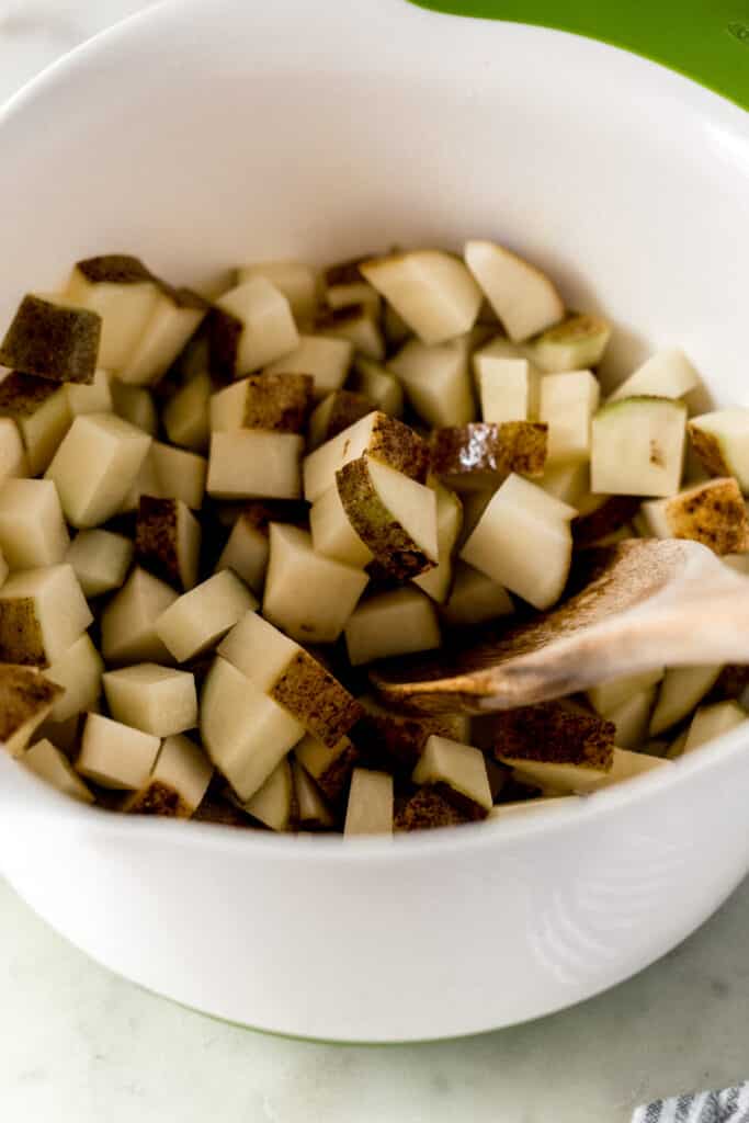 diced potatoes in a large white mixing bowl with wooden spoon