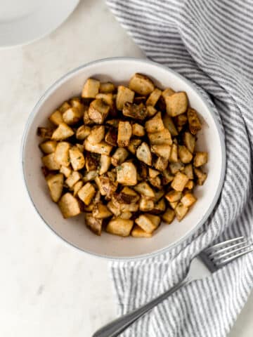 overhead view easy roasted potatoes in large white serving bowl with fork, plate, and napkin