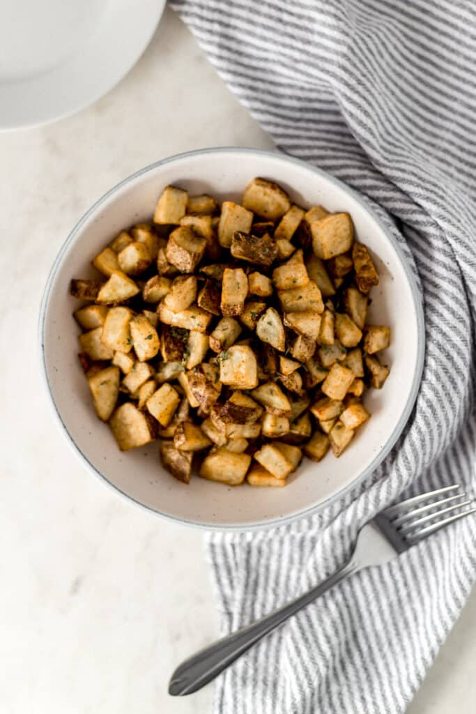 overhead view easy roasted potatoes in large white serving bowl with fork, plate, and napkin