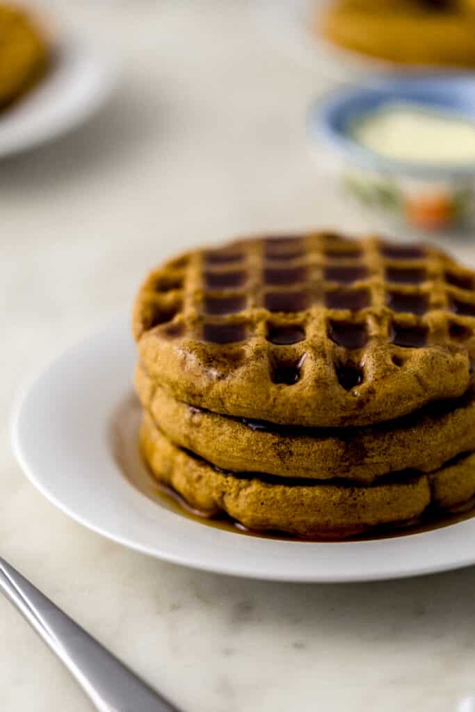 three waffles stacked on white plate topped with maple syrup. 