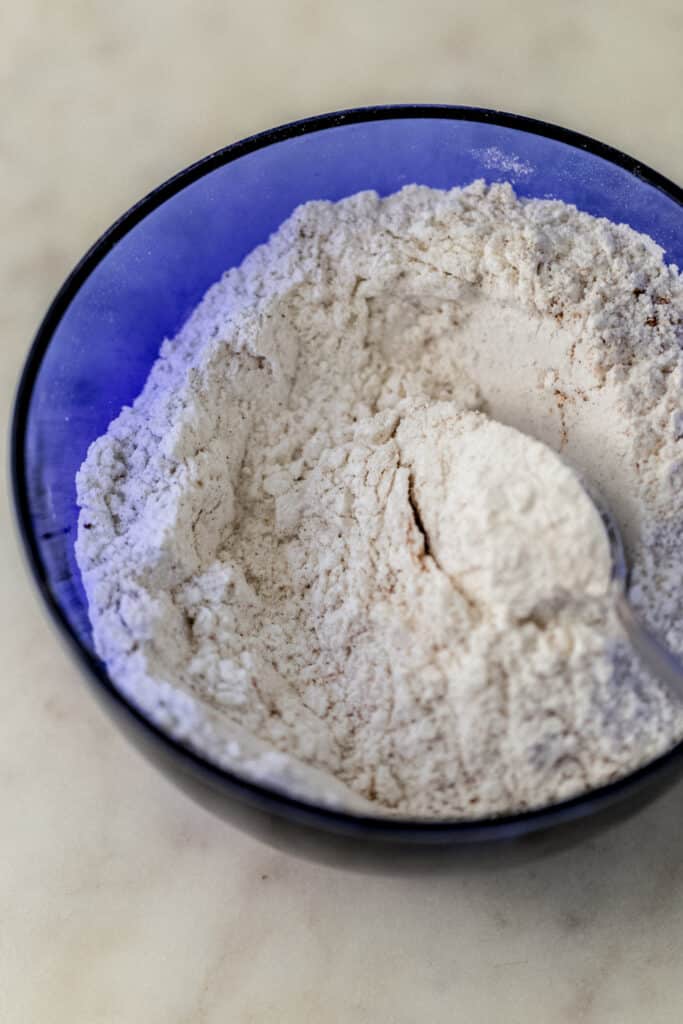 flour, baking powder, and pumpkin spice combine in blue bowl with spoon. 
