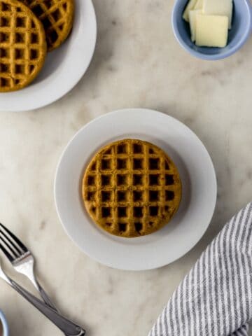 waffles on a small white plate with forks, cloth napkin, and small bowl with butter.