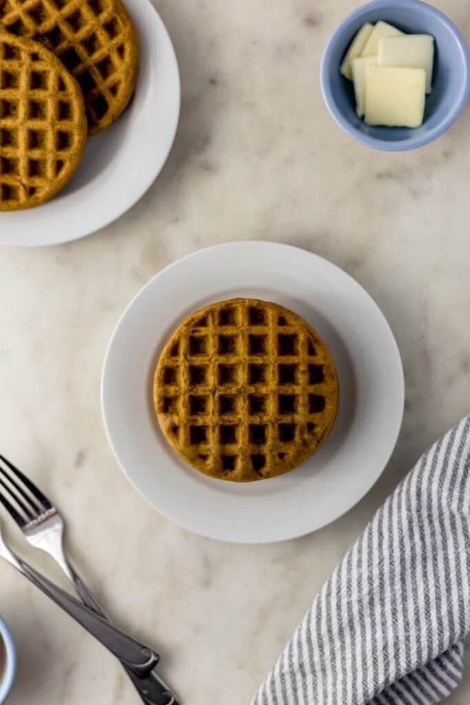 waffles on a small white plate with forks, cloth napkin, and small bowl with butter. 