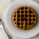 pumpkin spice latte waffle on white plate topped with syrup next to fork.