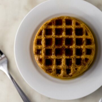 pumpkin spice latte waffle on white plate topped with syrup next to fork.