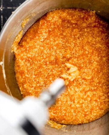 Overhead view of wet cake ingredients added to butter sugar mixture in stand mixer bowl.
