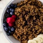 chocolate quinoa in white serving bowl topped with fresh berries, chocolate, and banana.
