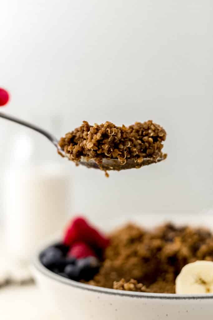 hand holding spoon with chocolate quinoa on it over bowl. 