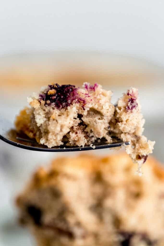 hand holding fork with blueberry coffee cake on it over plate