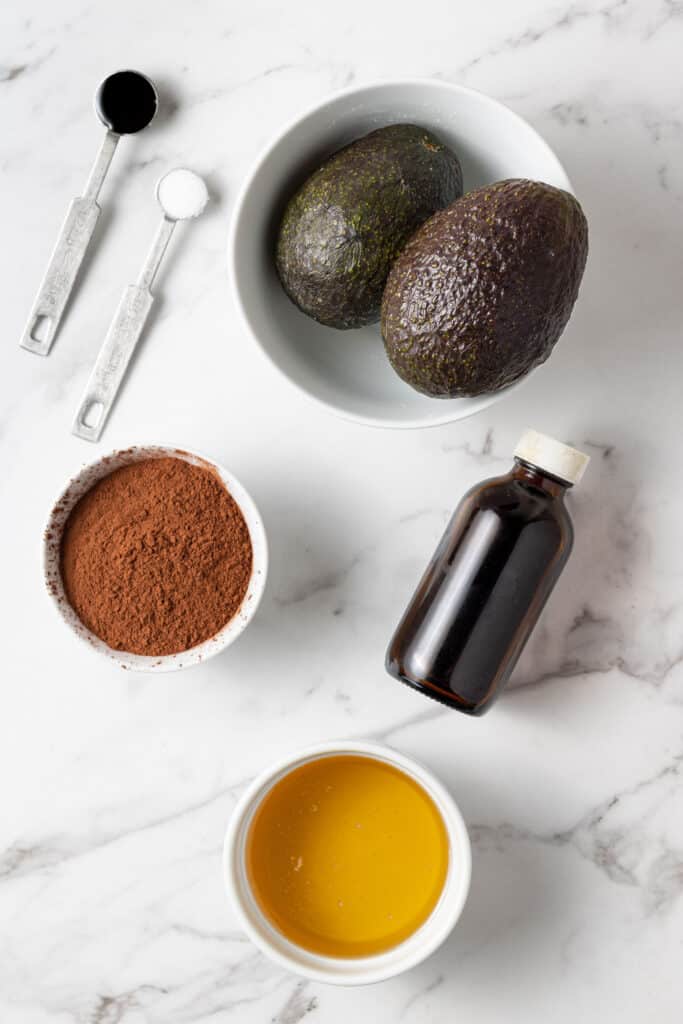 ingredients to make chocolate avocado mousse on marble surface. 