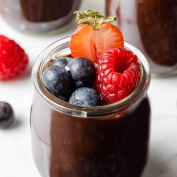 side view of chocolate avocado mousse in small glass jar topped with berries.