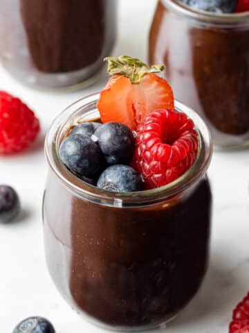 side view of chocolate avocado mousse in small glass jar topped with berries.