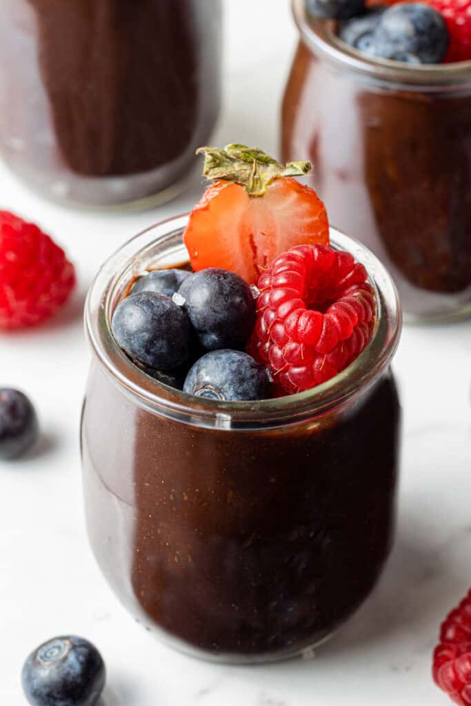 side view of chocolate avocado mousse in small glass jar topped with berries.