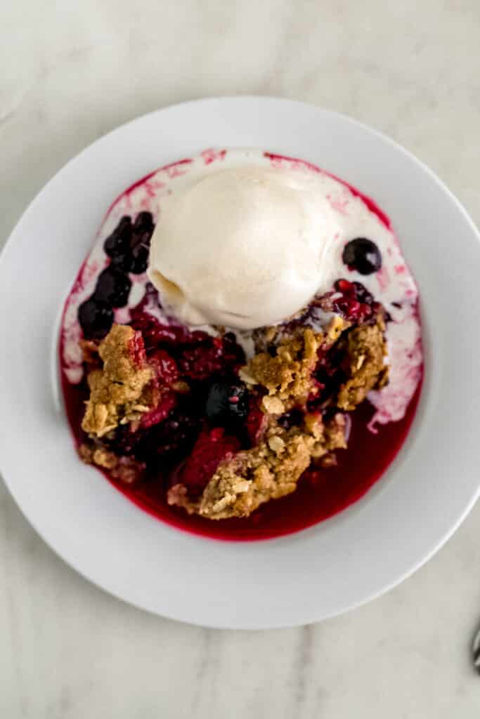 small white plate with serving of berry crisp with vanilla ice cream 