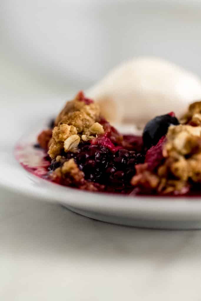 close up side view serving easy berry crisp with ice cream on white plate