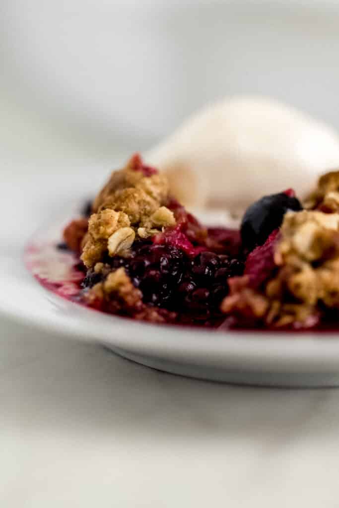 close up side view serving easy berry crisp with ice cream on white plate