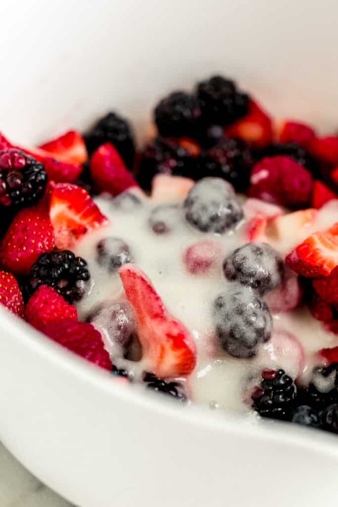 close up side view berries in white mixing bowl with sugar mixture 