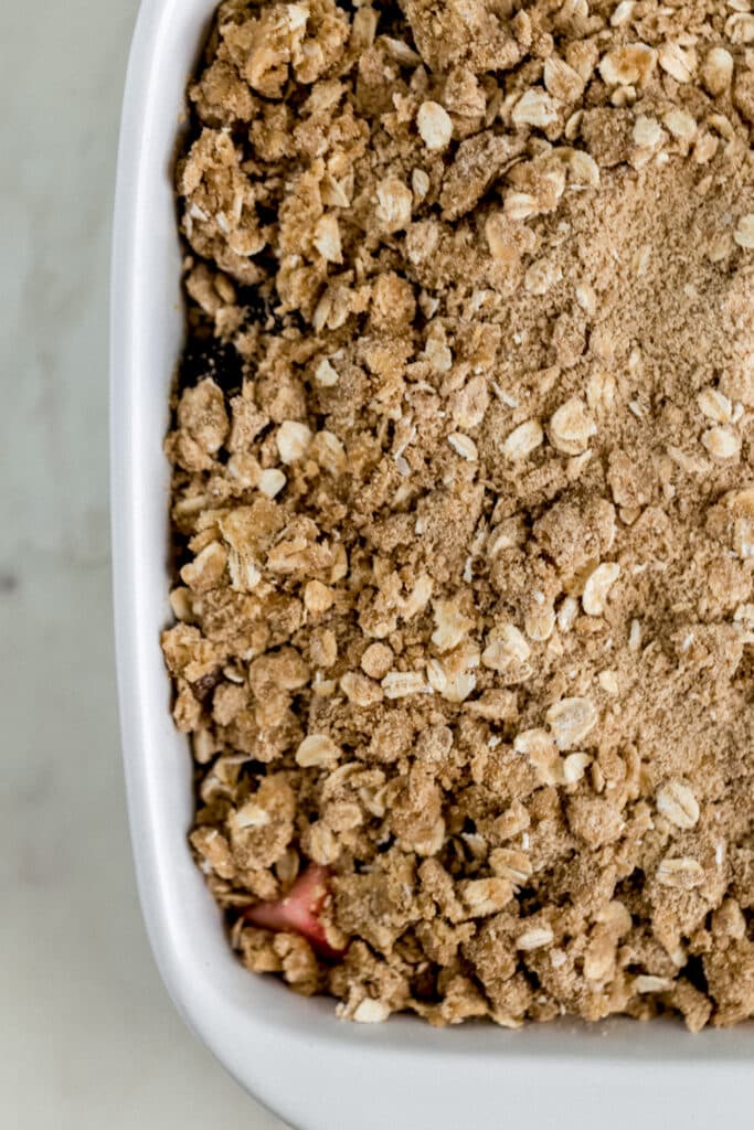 crisp topping over berry mixture in white baking dish 