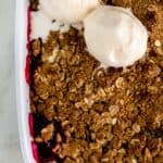 berry crisp in square white baking dish with two scoops of vanilla ice cream on top