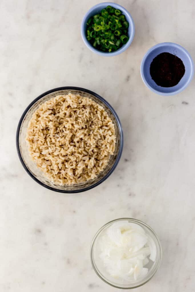 ingredients for fried brown rice in small bowls on marble surface 