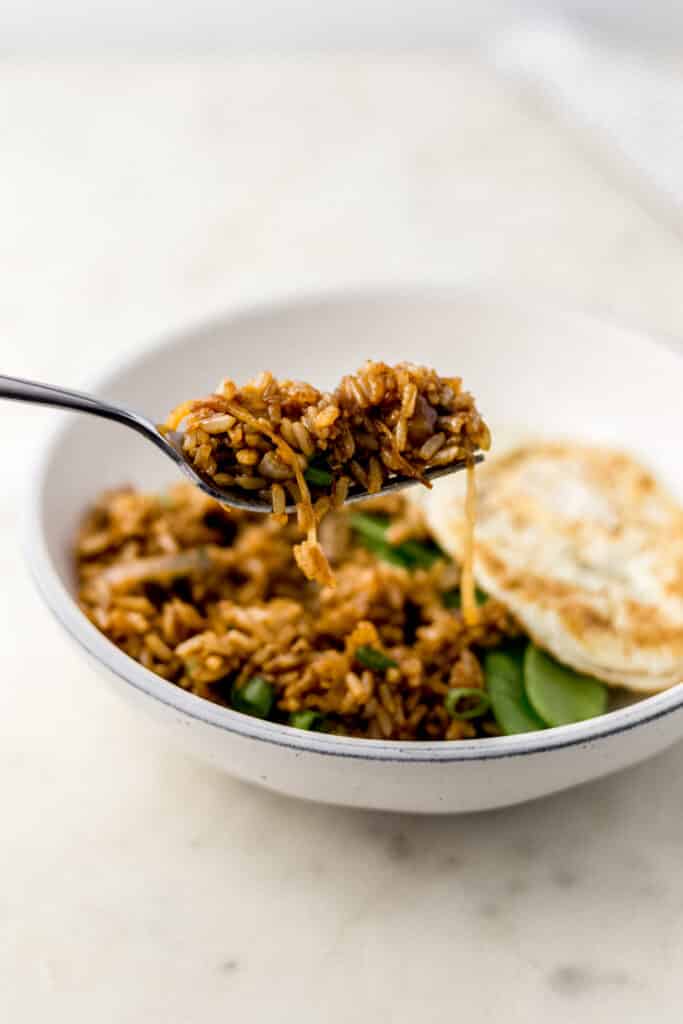 hand holding fork with fried brown rice on it over bowl 