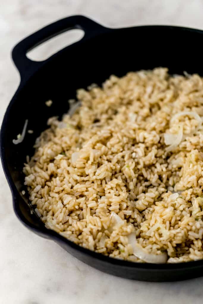 fried brown rice with onion, garlic, and ginger in cast iron skillet 