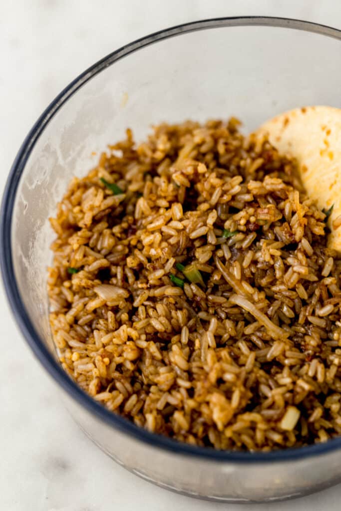 cooked fried brown rice in glass bowl with wooden spoon 