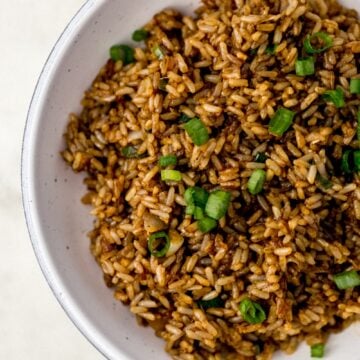 fried brown rice topped with green onion in white serving bowl