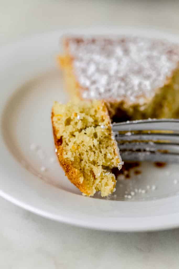 piece of orange olive oil cake on small white plate with fork