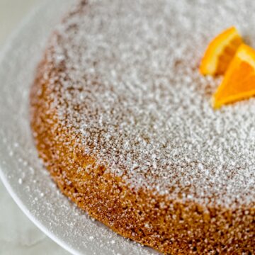 whole olive oil cake on big white plate topped with powdered sugar