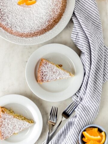 orange olive oil cake on three white plates with forks and napkin