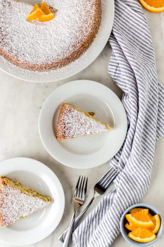 orange olive oil cake on three white plates with forks and napkin 
