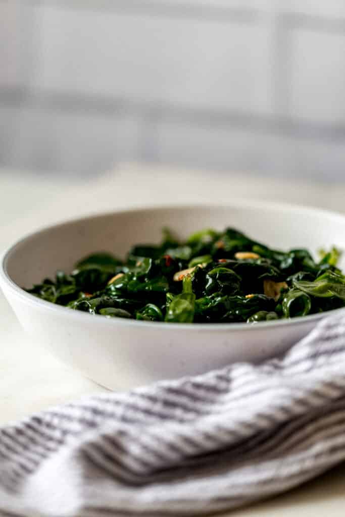side view sauteed garlic spinach in a white bowl next to a napkin