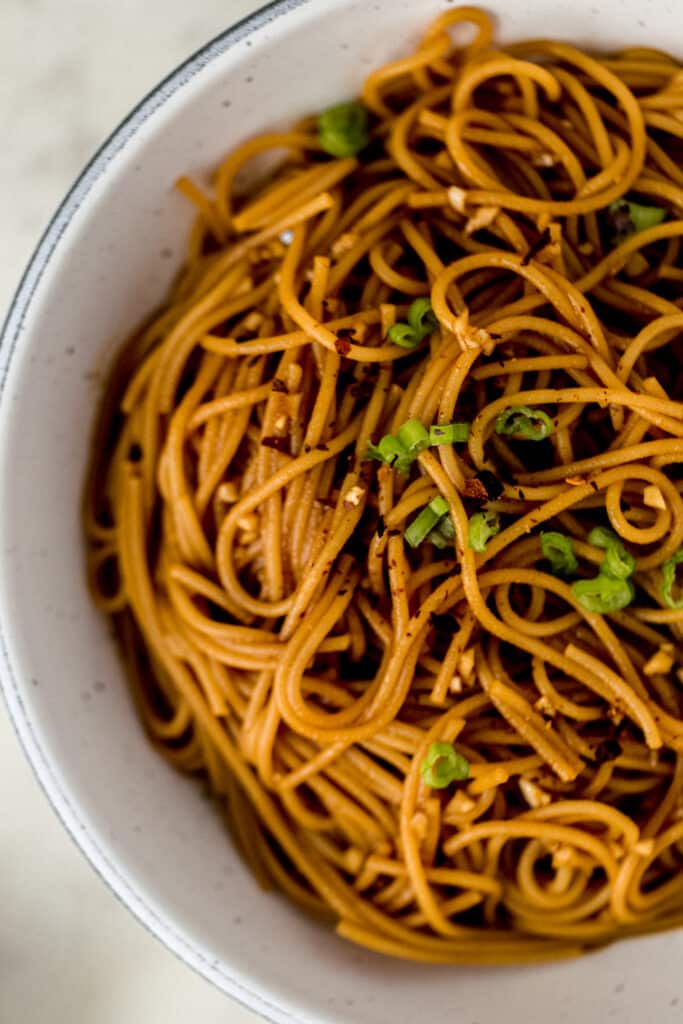 sesame noodles in large white bowl topped with green onions