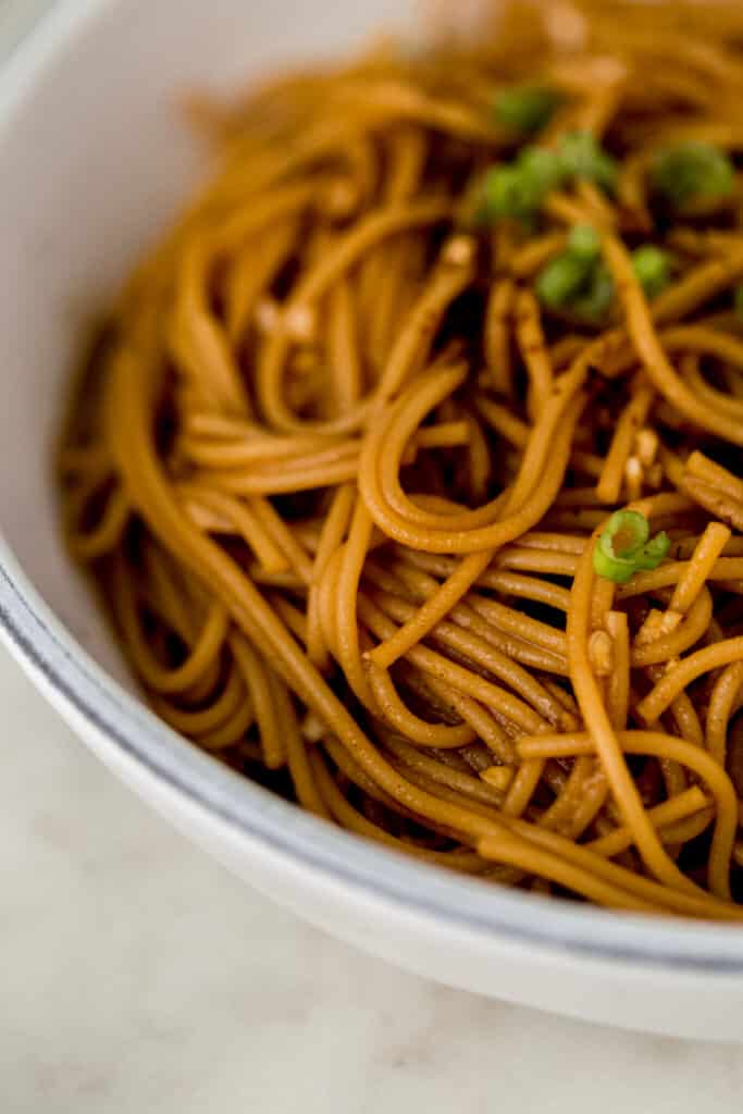 close up side view sesame noodles in large white bowl topped with scallions