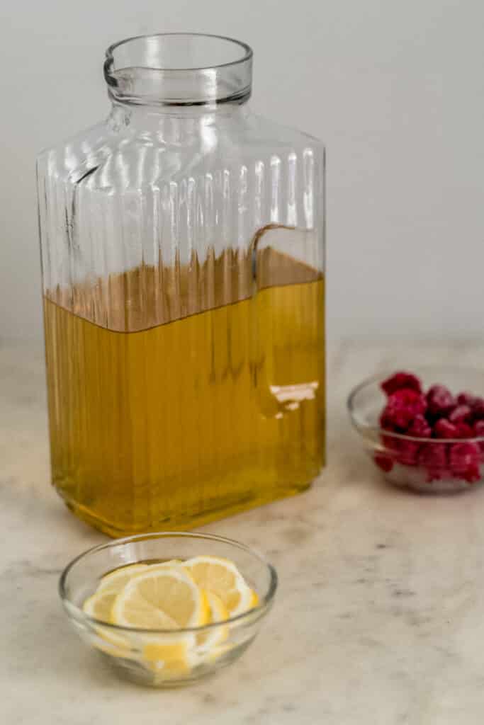 green tea in glass pitcher with small bowls of lemon and raspberries 